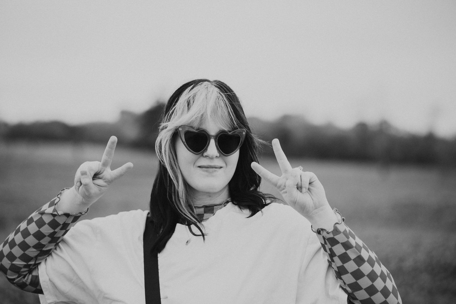 Black and white portrait of a woman in sunglasses making peace signs.