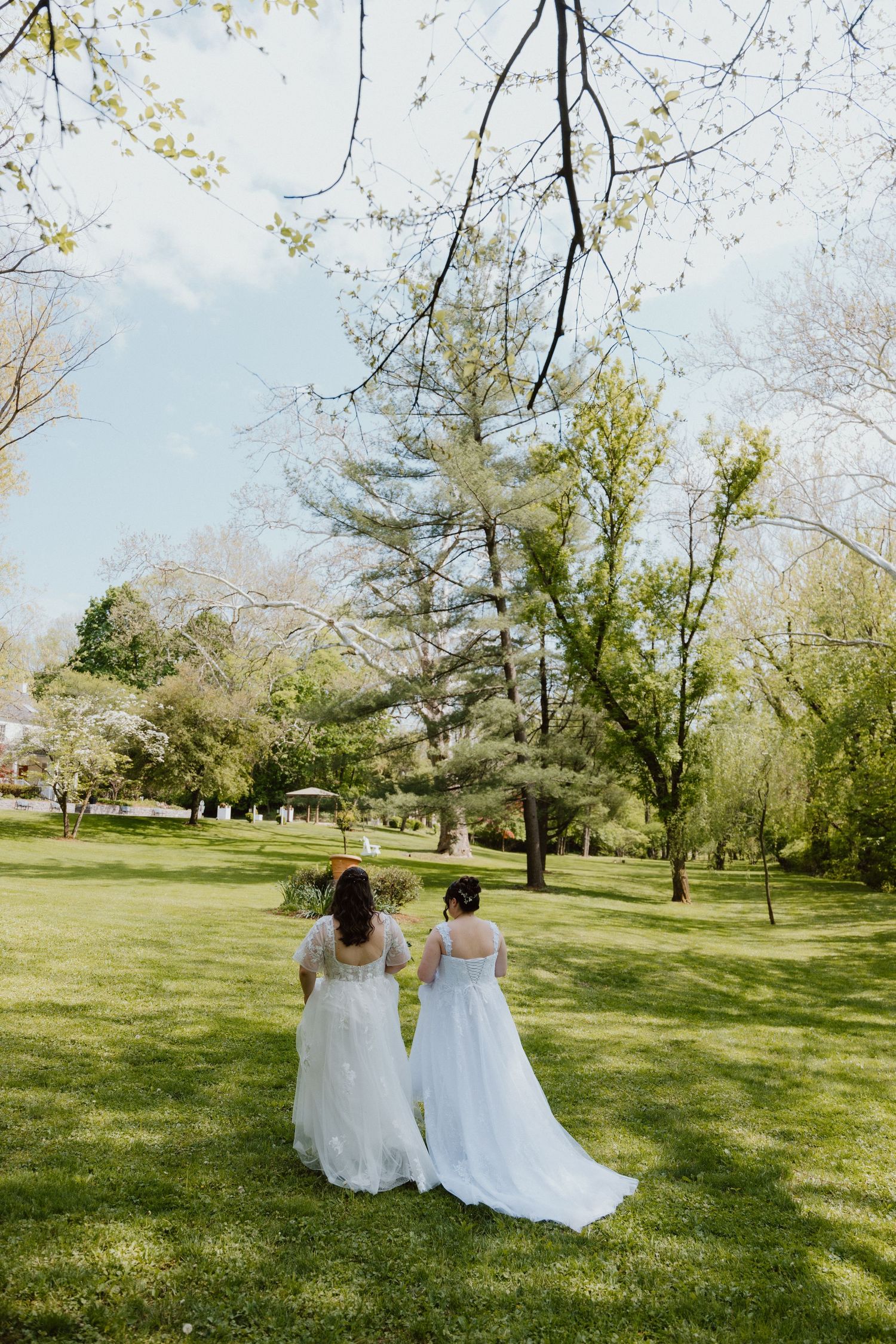 Two brides standing together under a tree in a garden during an outdoor wedding.