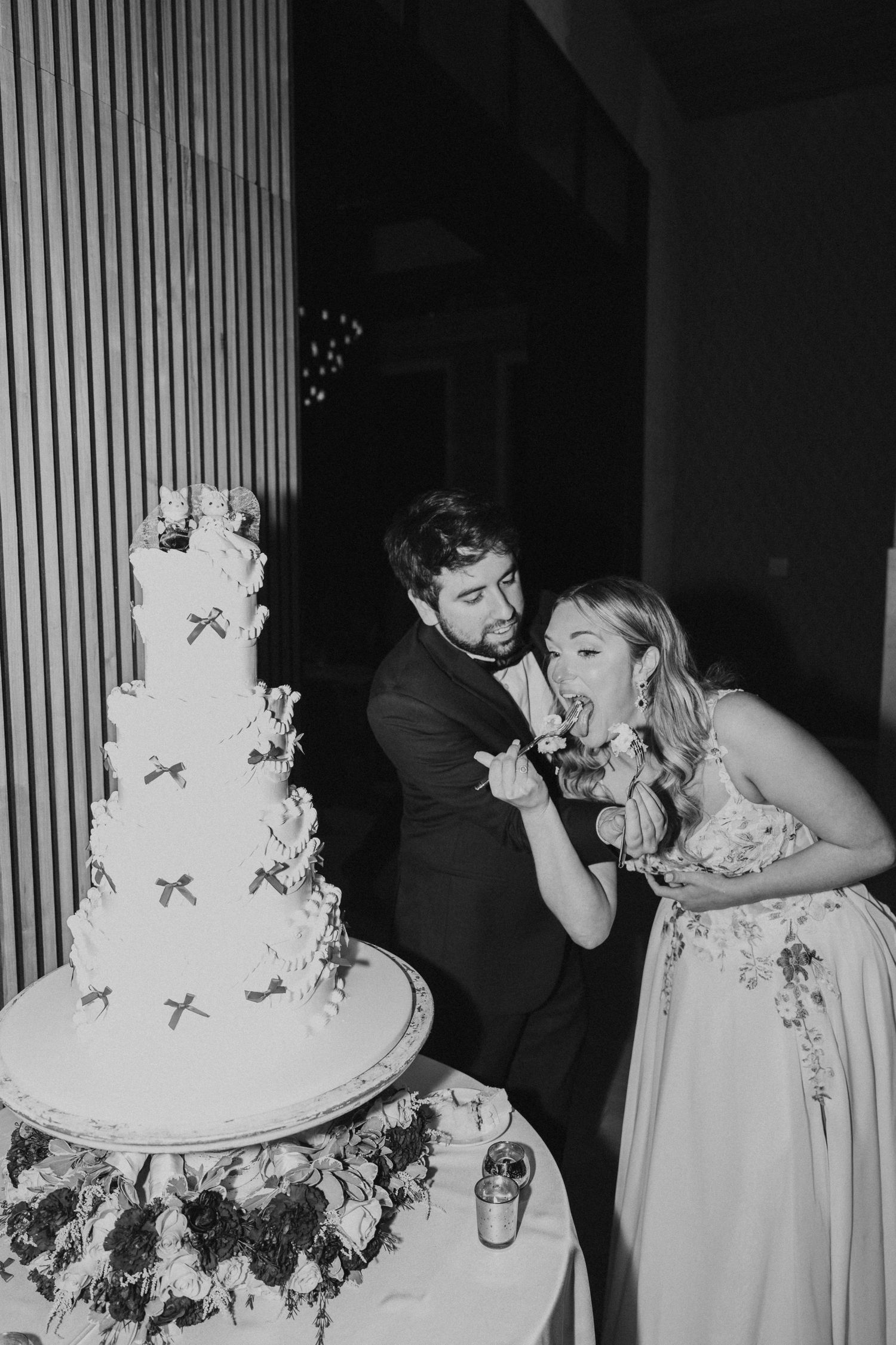 Black and white photo of a bride and groom cutting their tiered wedding cake together.