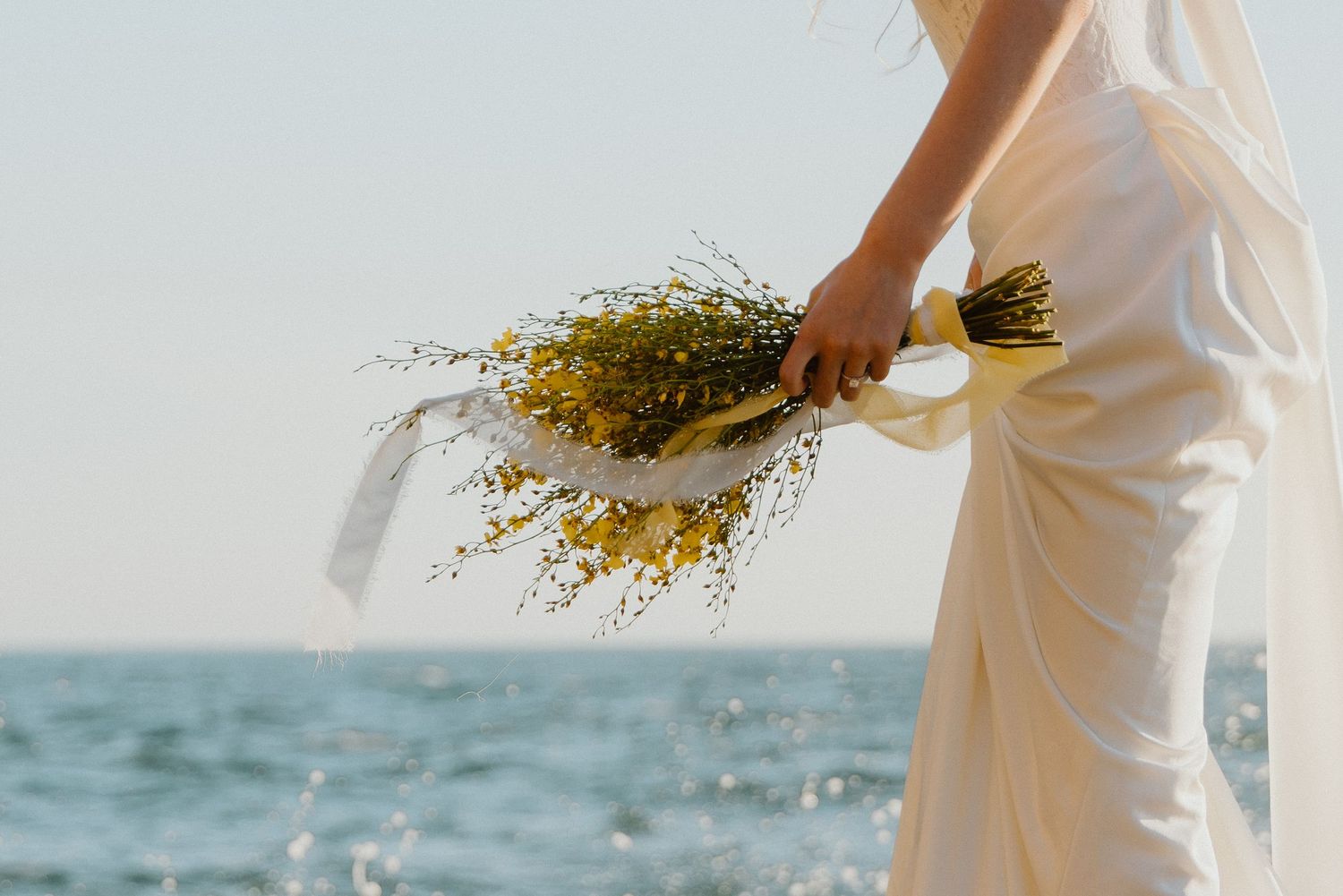 Bride holding a wildflower bouquet by the ocean during a coastal elopement.