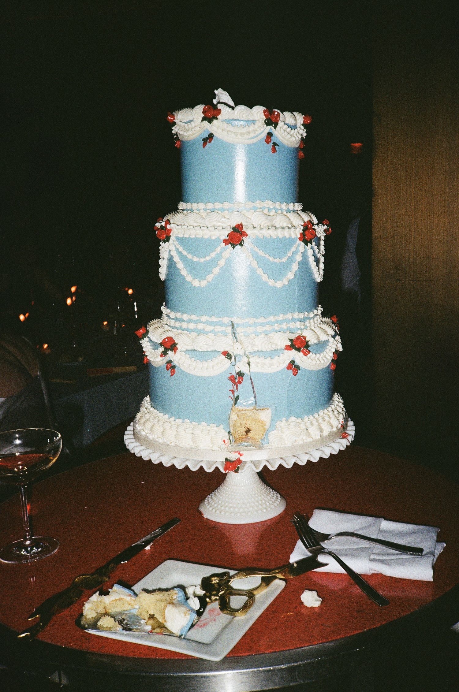 Tiered blue wedding cake with white piping details displayed on a stand at a vintage-inspired reception.