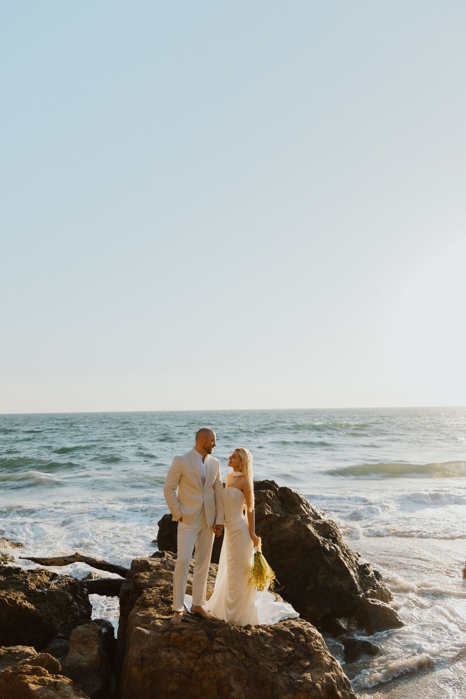 Couple standing on coastal rocks overlooking the ocean during a seaside elopement.