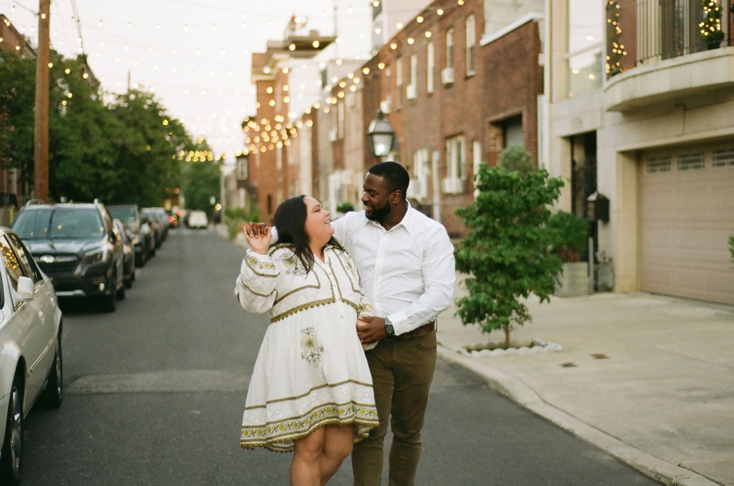 Couple walking together along a sunlit cobblestone street during an urban engagement session.