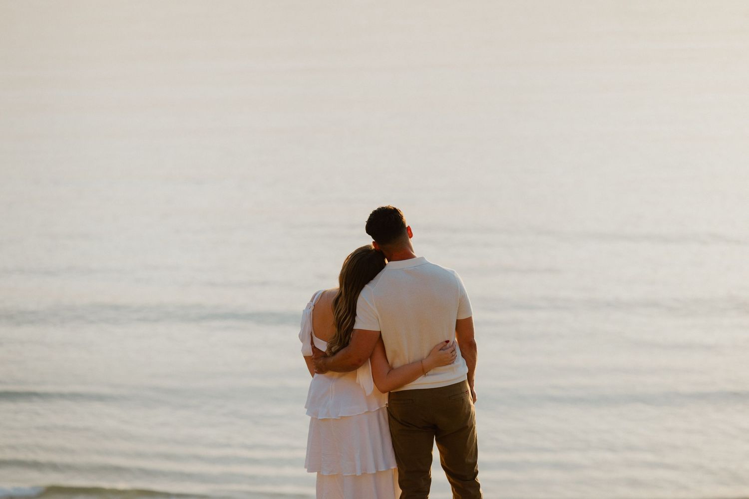 Couple embracing as they look out over the ocean at sunset during a beach elopement.