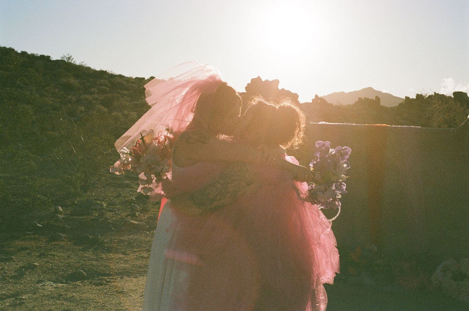 Bride and groom embracing in a grassy field with the sun behind them during an outdoor wedding.