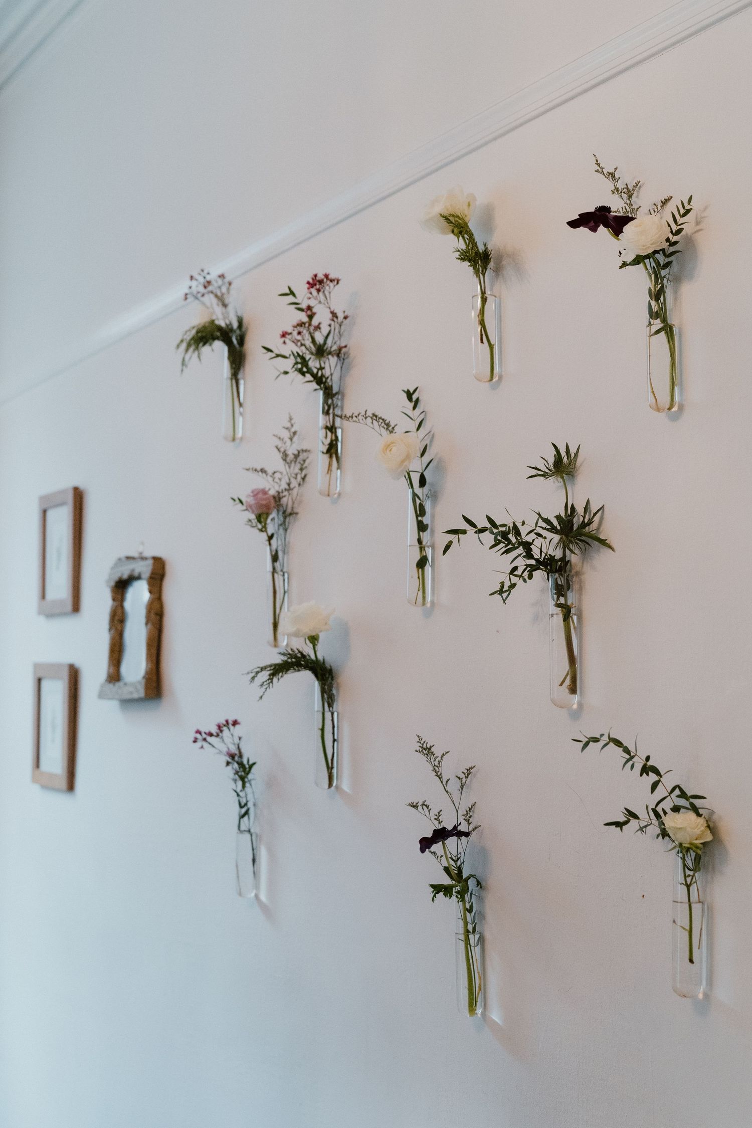 Row of hand-tied wedding boutonnieres displayed on a white wall before being pinned on groomsmen.