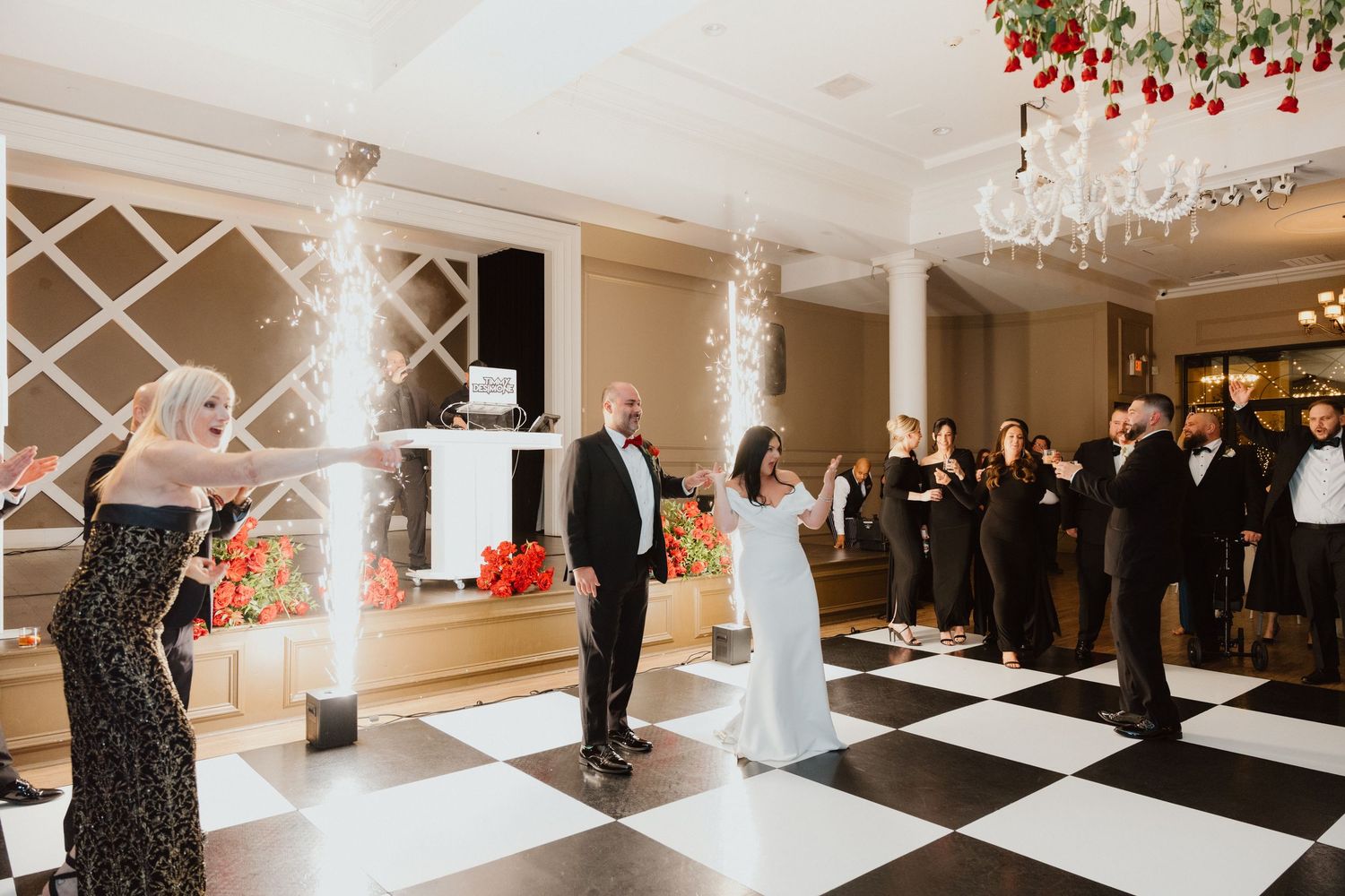 Wedding guests mingling on a black and white checkered ballroom floor beneath an ornate chandelier.