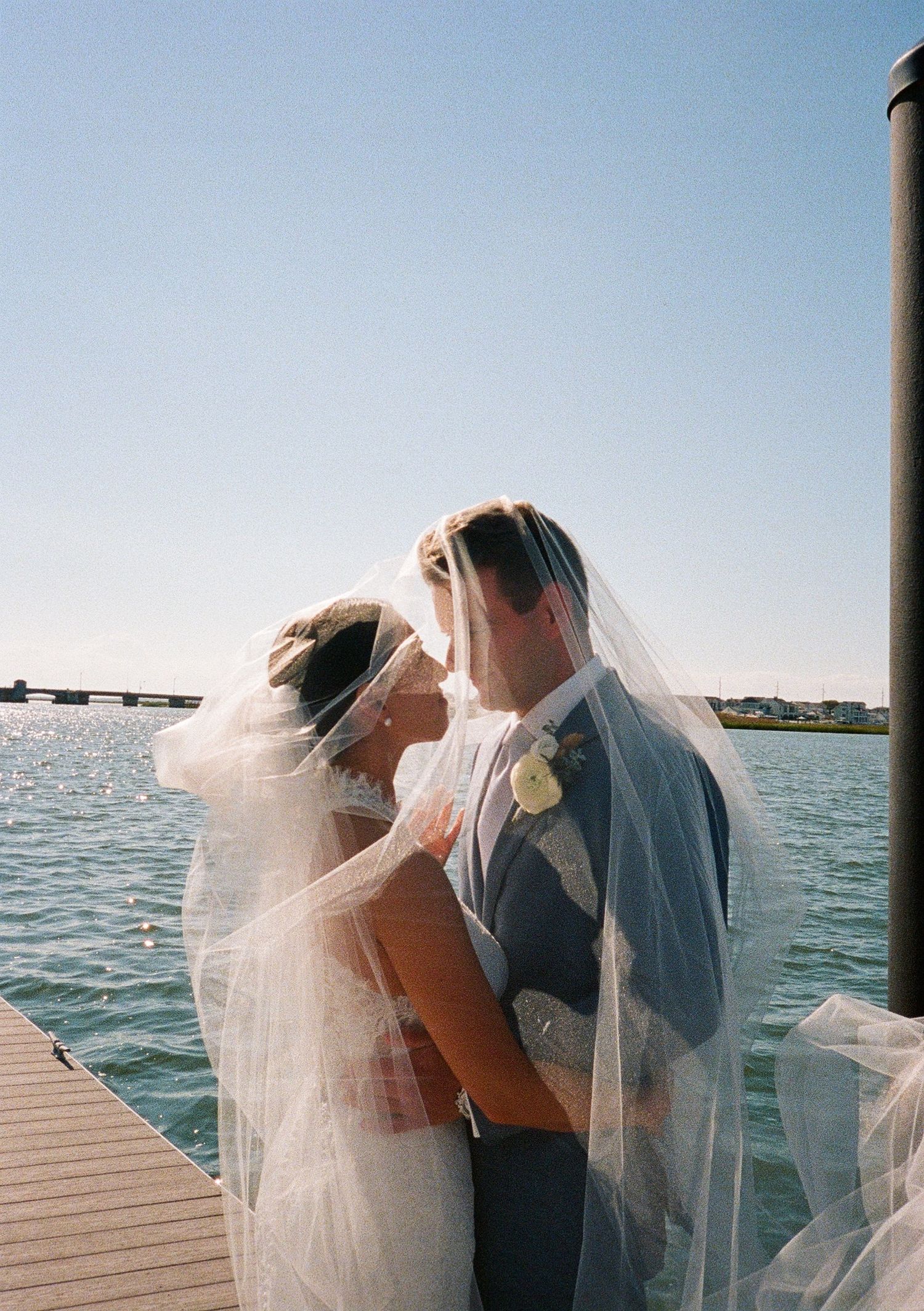 Bride and groom kissing under a veil at a waterfront elopement.