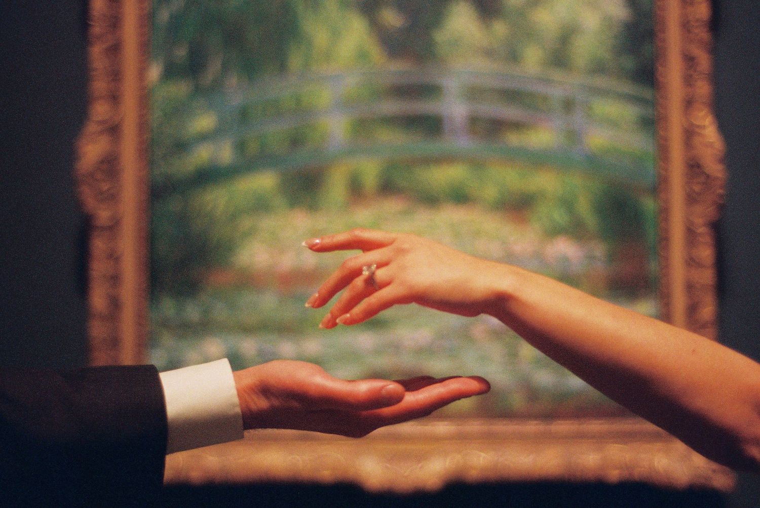 Two hands reaching toward each other before a framed painting.