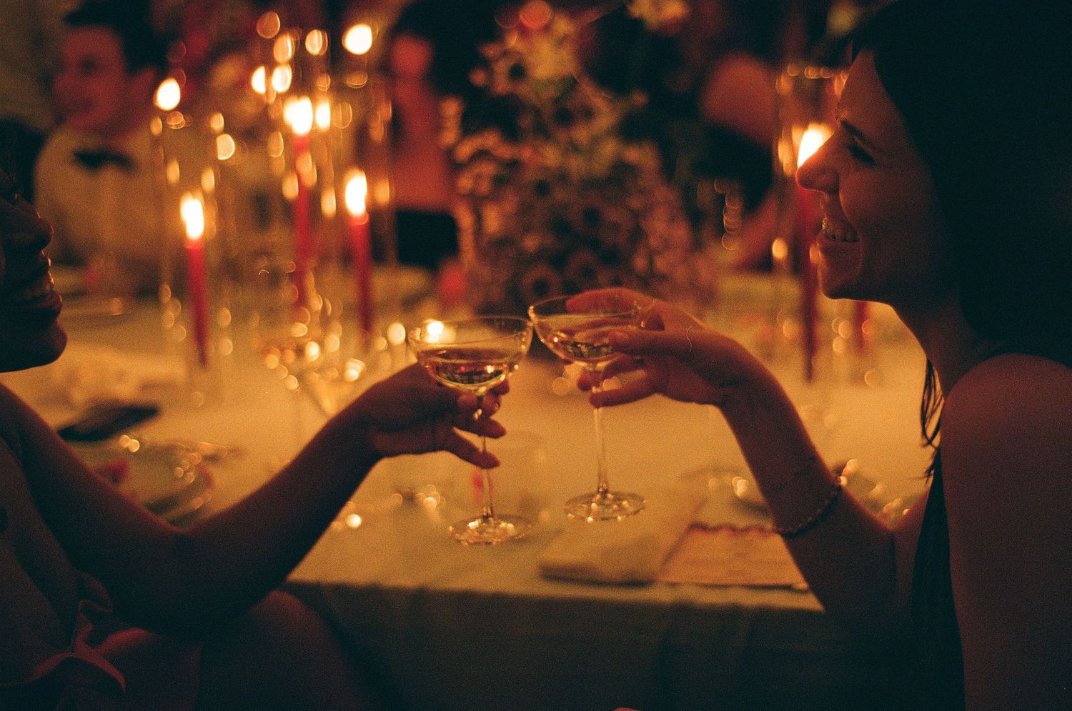 Hand reaching for a glass over a candlelit reception table aglow with warm twinkling lights.