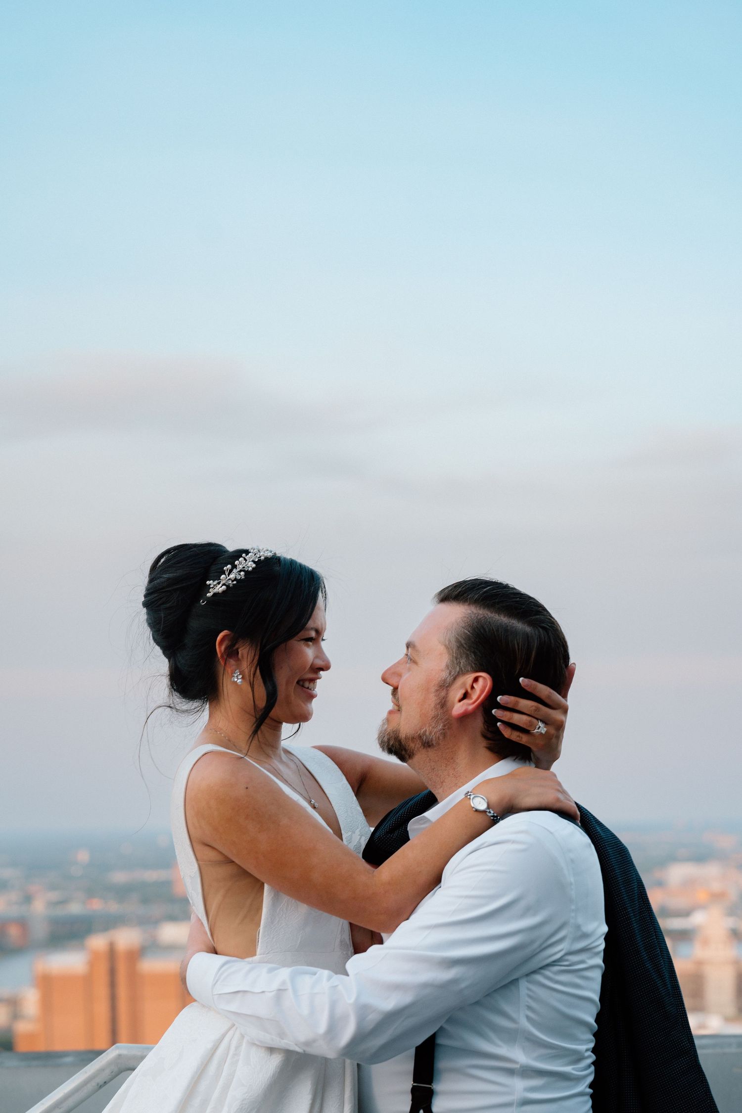 Bride and groom kissing on a rooftop terrace with city views behind them.