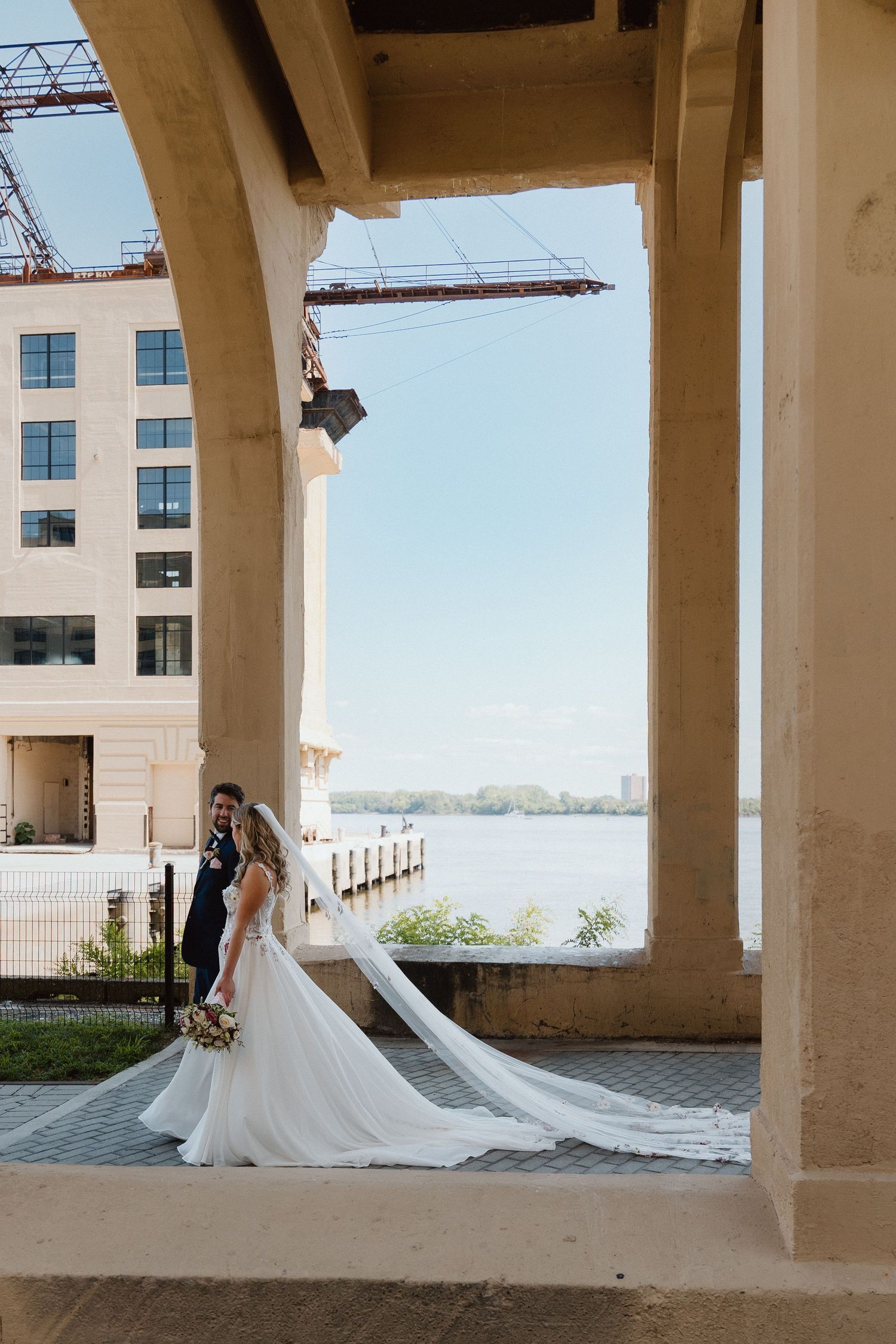 Bride with a long flowing train framed by a stone archway with light streaming through.