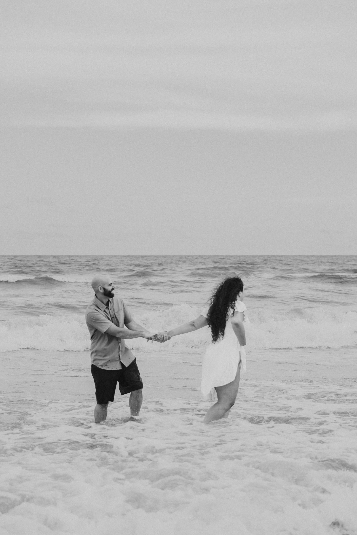 Black and white photo of a couple holding hands in the ocean during a beach elopement.