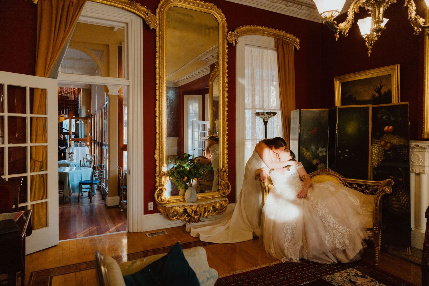 Bride and groom in an intimate embrace inside a grand historic mansion with crimson walls and antique details.
