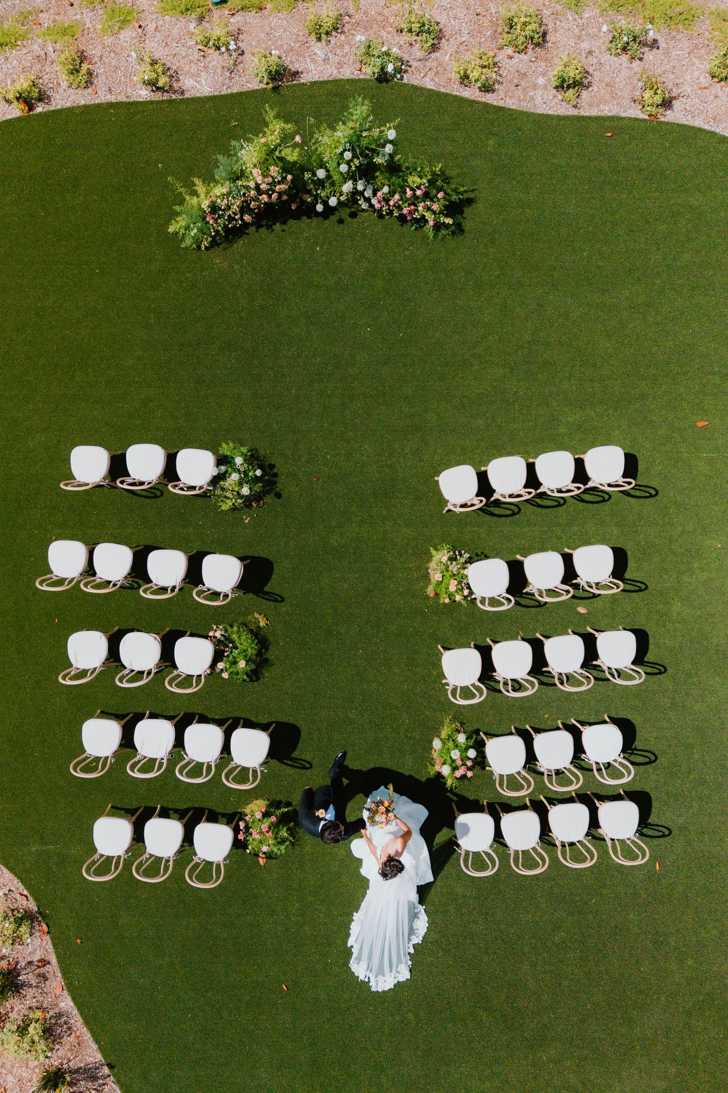 Aerial view of an outdoor wedding reception with tables arranged on a green lawn.
