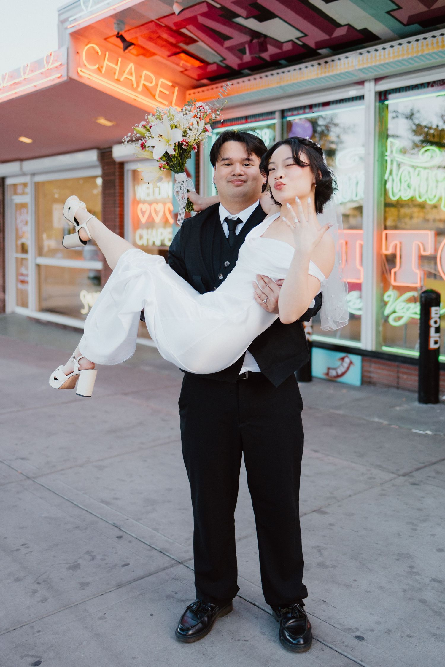 Groom lifting his bride in his arms on a city street outside a storefront.