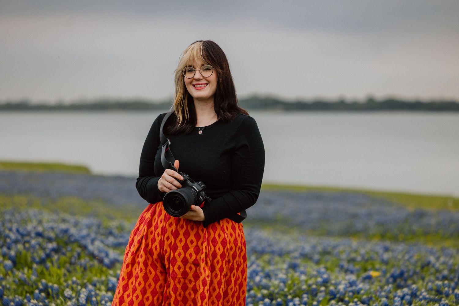 Photographer standing in a field of bluebonnets holding a camera.