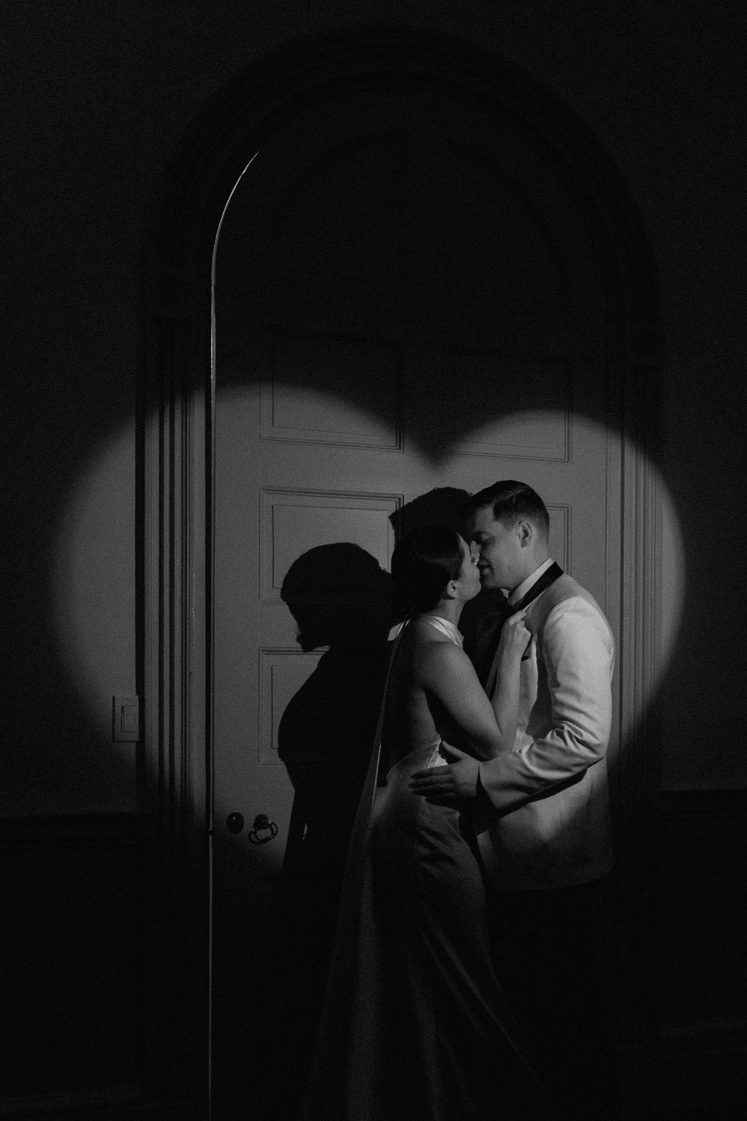 Silhouette of a couple kissing beneath an arched doorway in dramatic black and white.