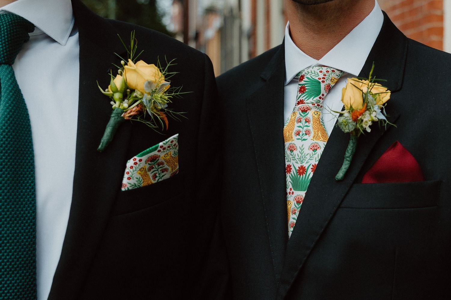 Two grooms in suits with floral boutonnieres at a wedding.