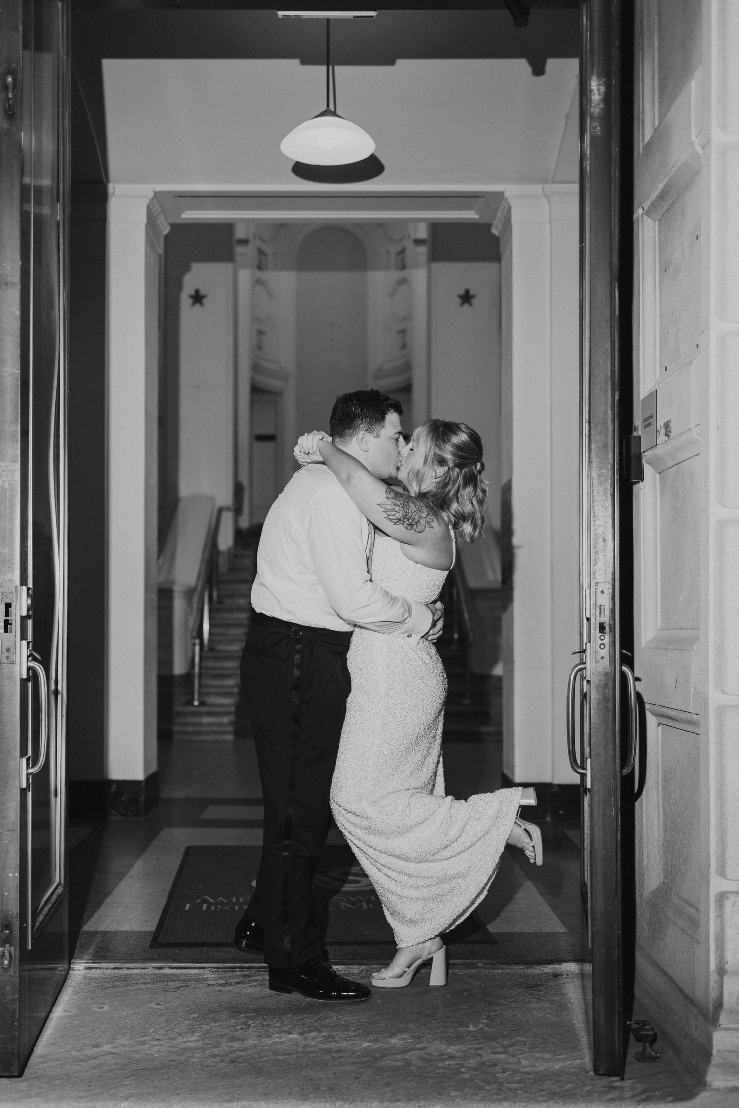 Black and white photo of newlyweds kissing in a doorway.