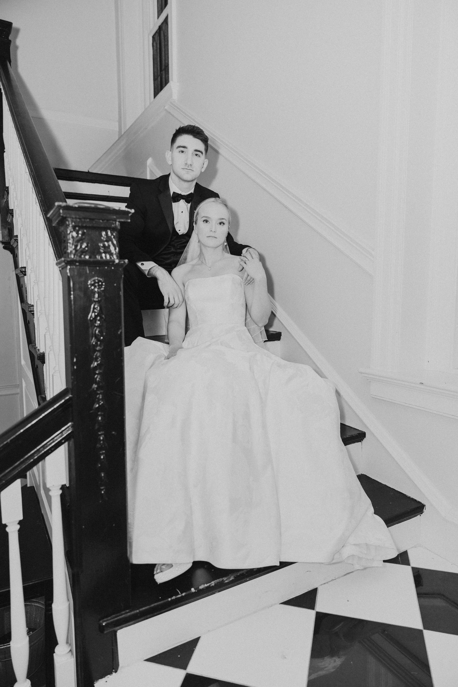 Dramatic black and white photo of a bride with a long train walking down a sweeping grand staircase.