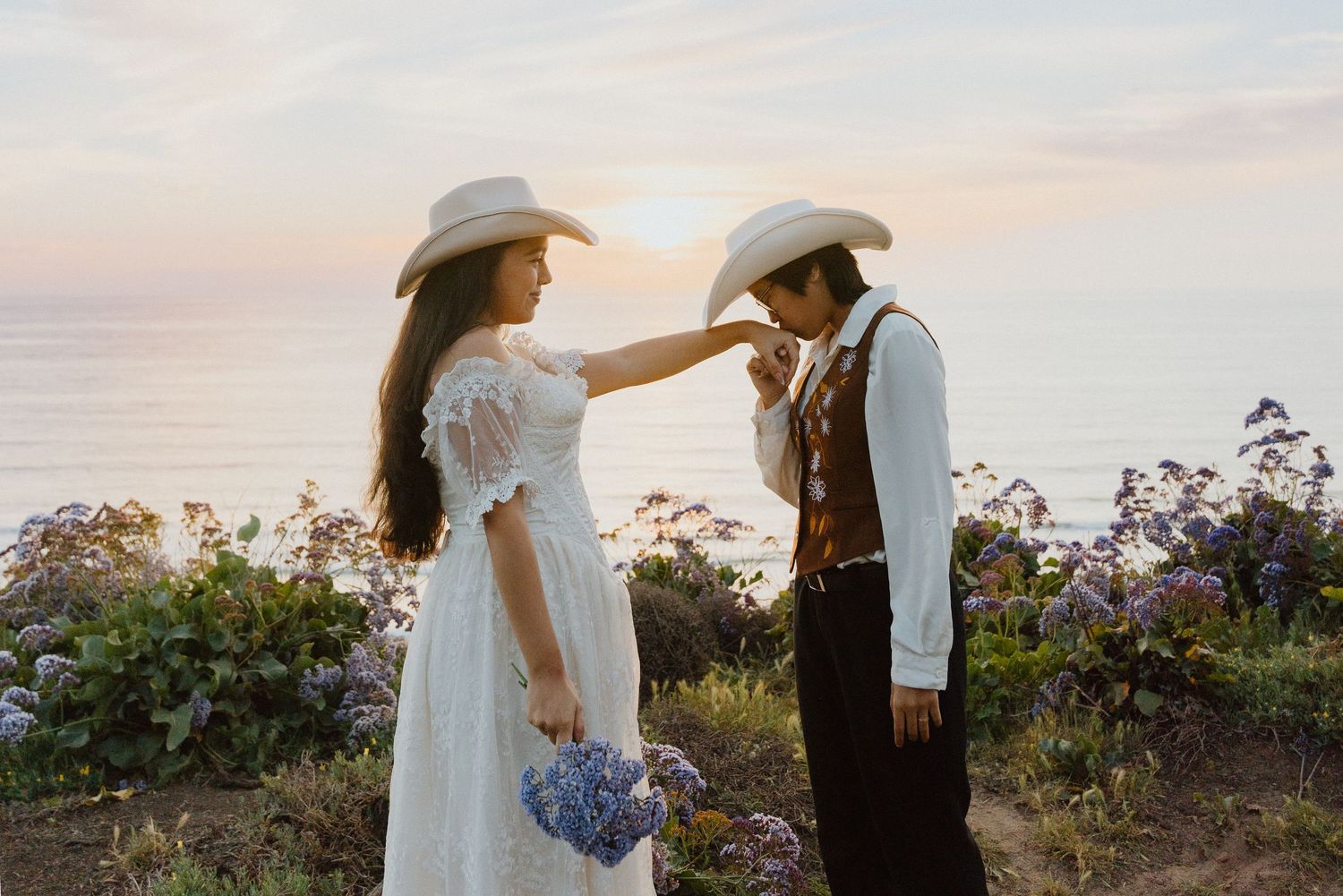 Bride and groom in western attire sharing a cowboy hat at sunset during a wildflower elopement.