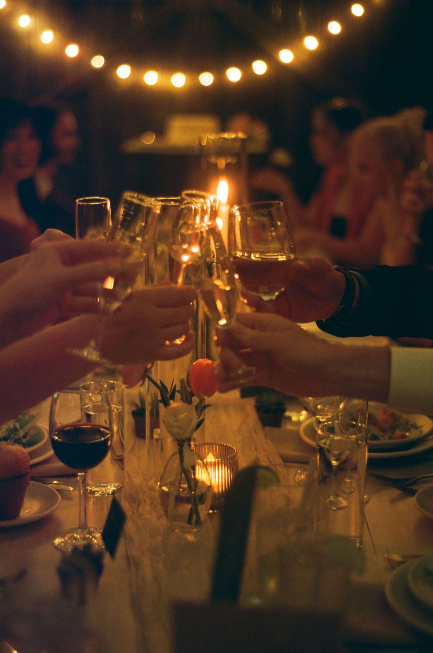 Outdoor evening wedding reception glowing with string lights over candlelit tables.