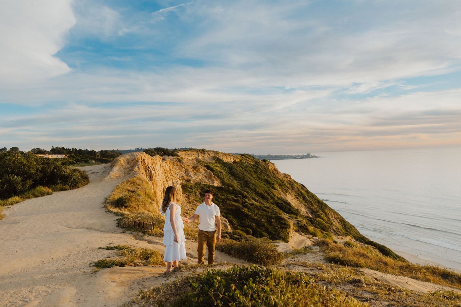 Couple walking along a coastal cliff at sunset during an oceanfront elopement.