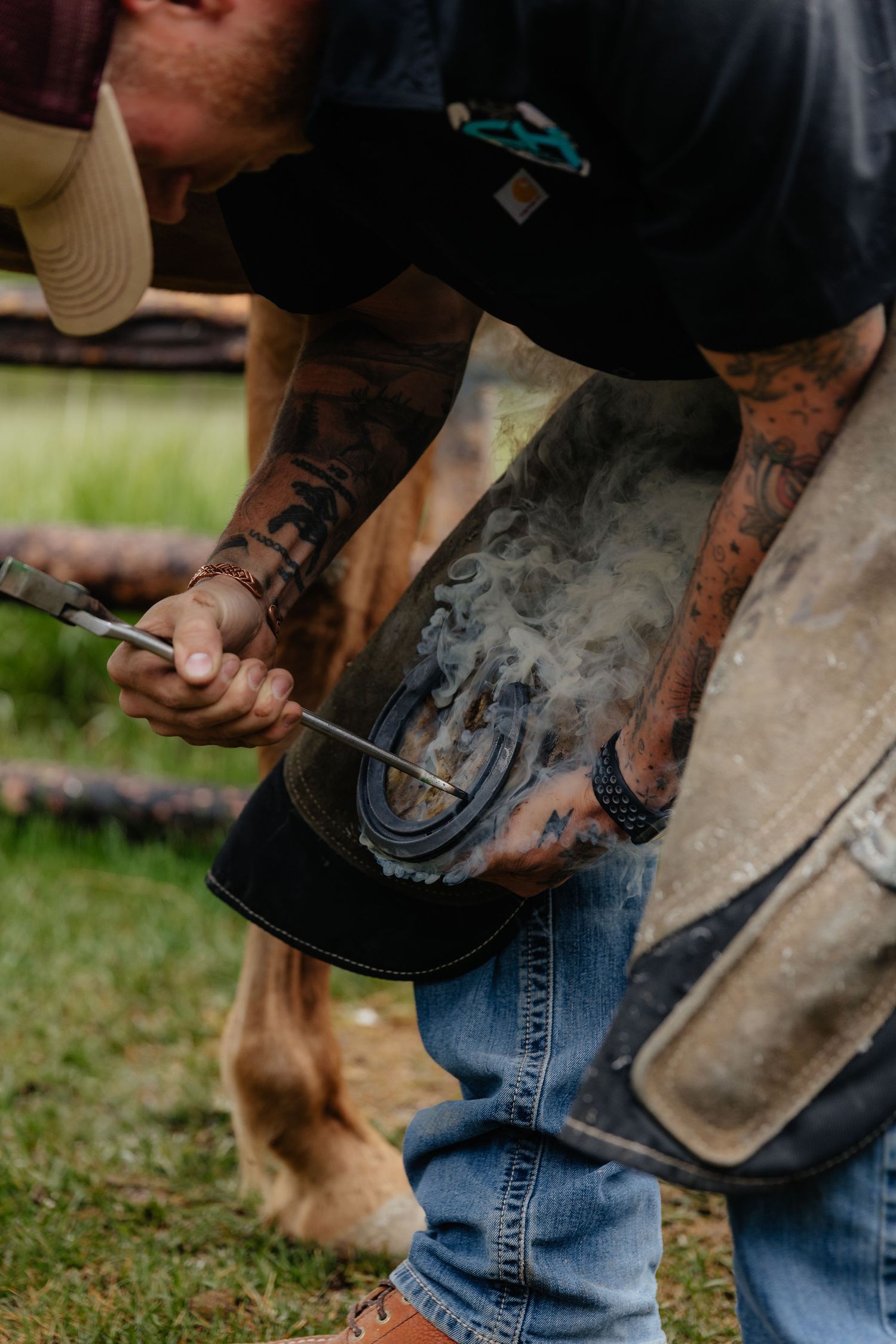 a farrier burning a horse shoe on a horse in island park for a marketing photoshoot with smoke coming off of the tools and horse hoof.