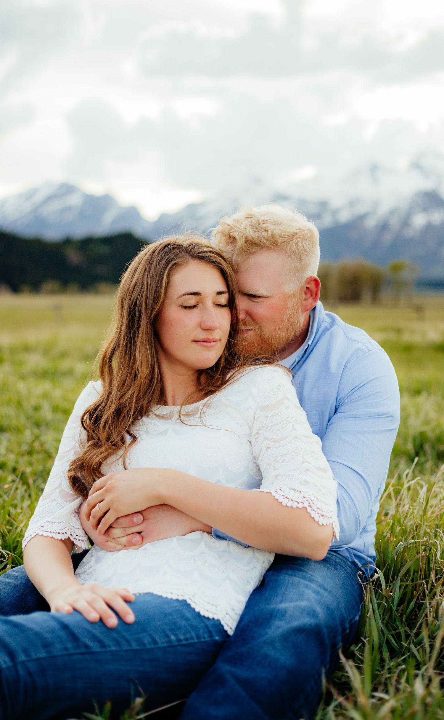 a cute couple posing for their engagement pictures in front of the Teton mountains in a field close to Jackson hole Wyoming.