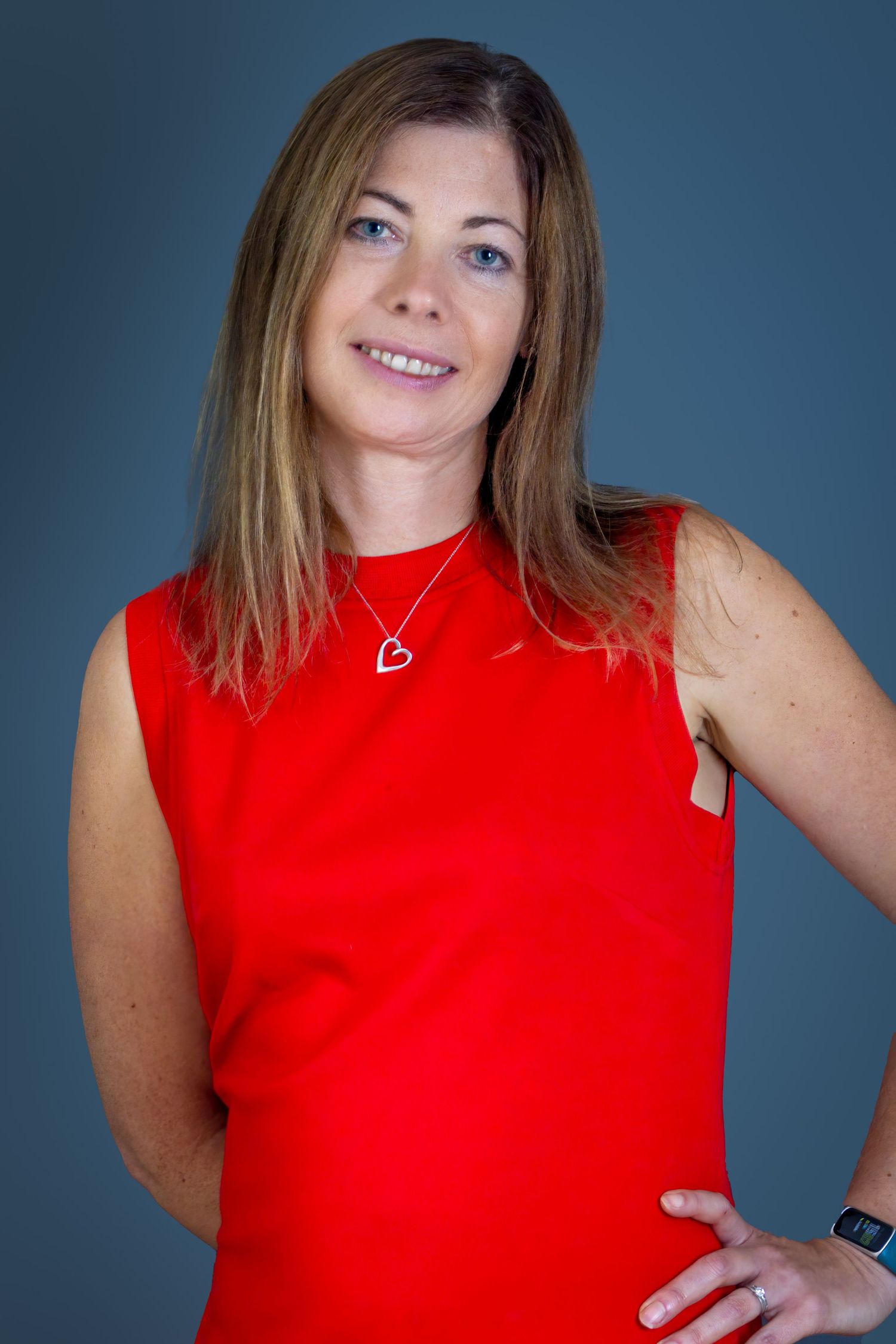 Professional studio portrait of someone in a vibrant red sleeveless top against a blue-grey background.