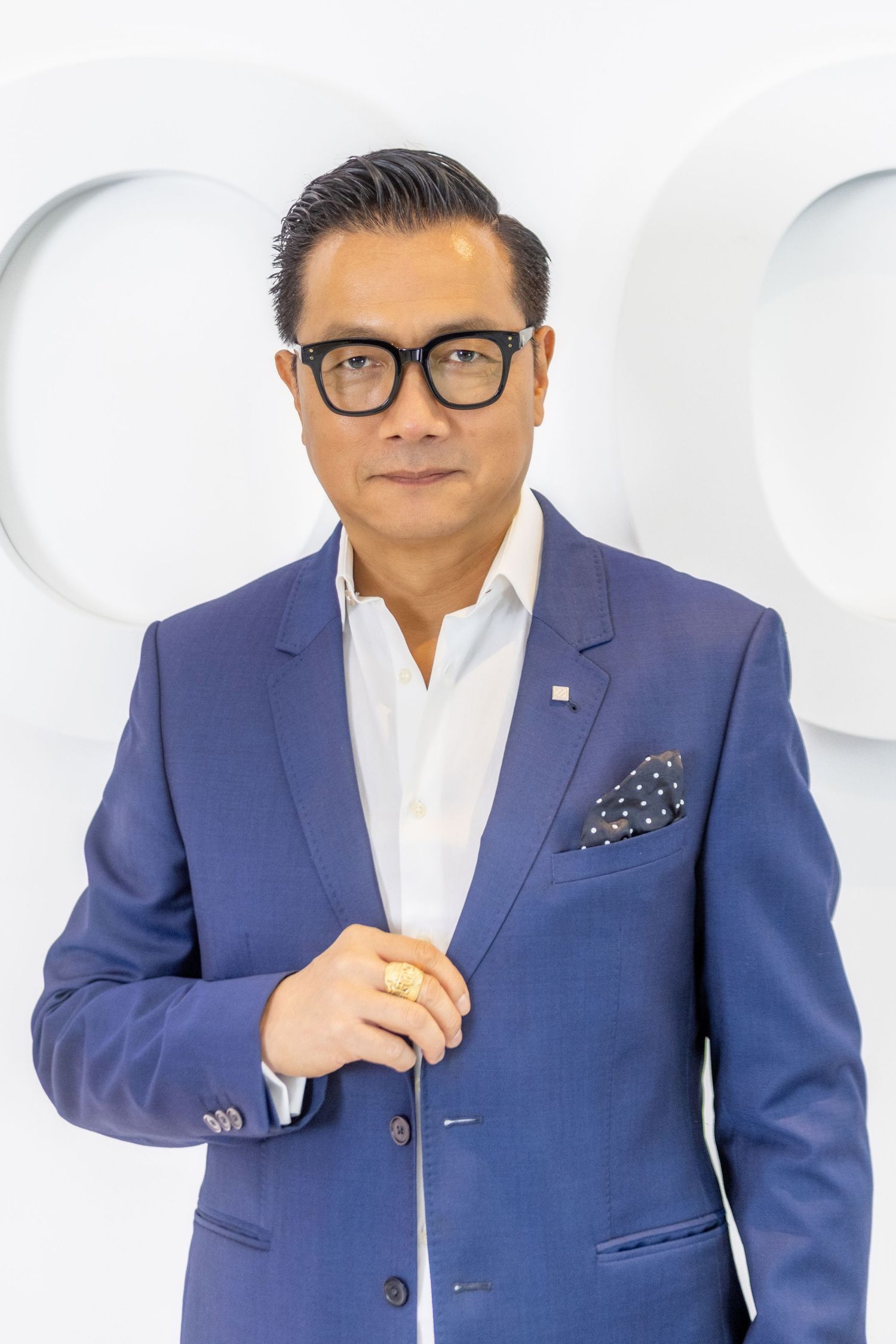 Professional portrait of Chinese man wearing a navy blue blazer, white dress shirt, patterned pocket square and black glasses.