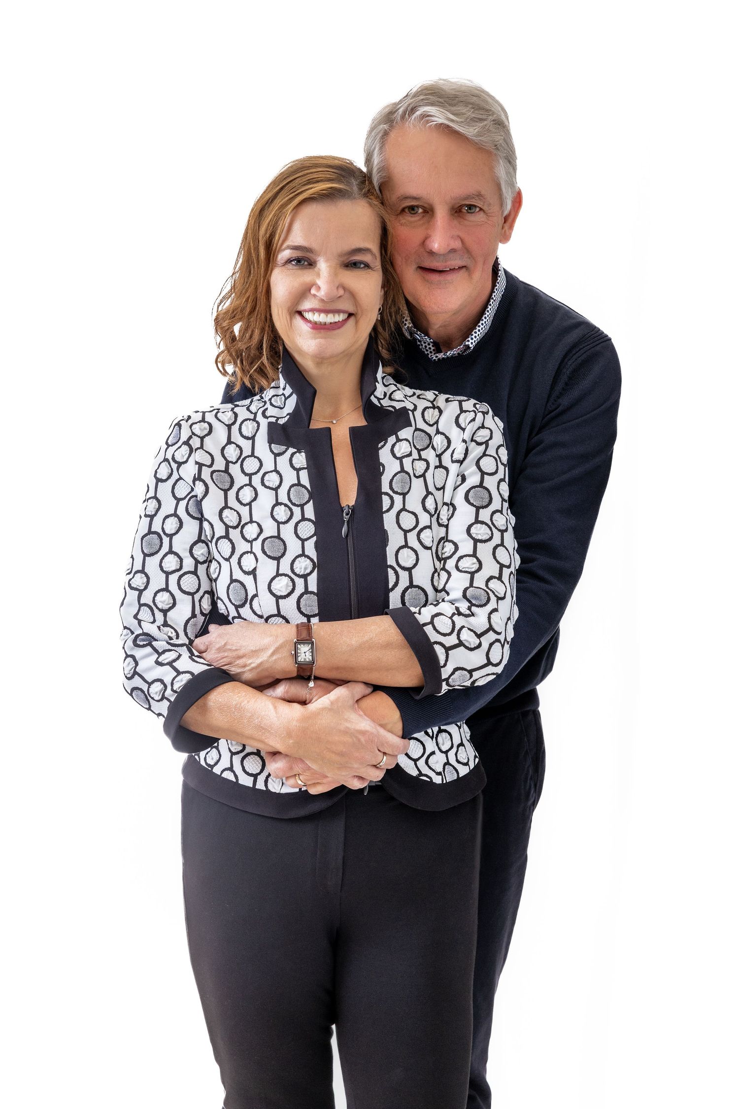 Professional photo of couple in coordinating outfits with black and white patterned jacket against white backdrop.