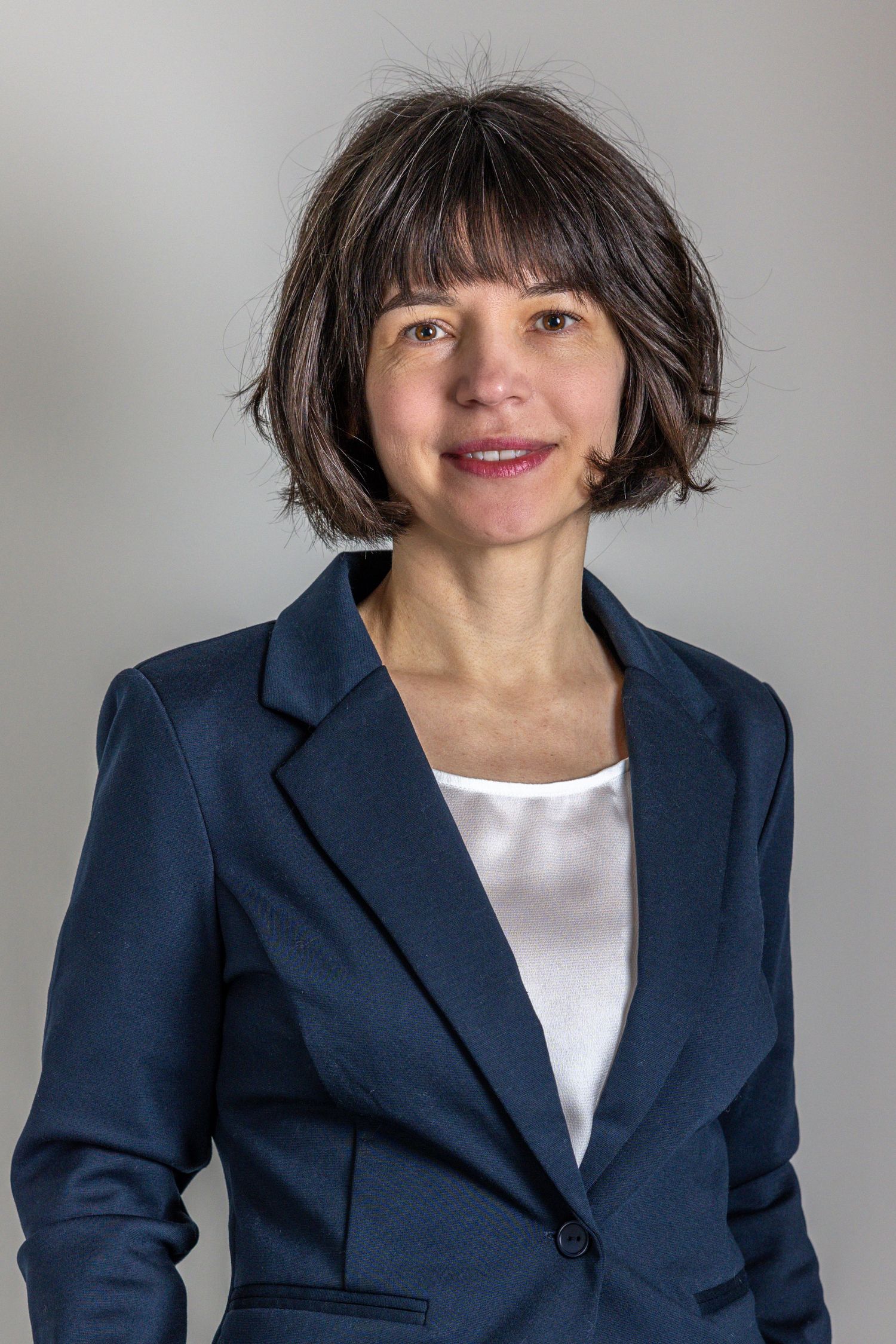 Professional business portrait of someone in a navy blazer and white blouse with a short dark bob hairstyle.