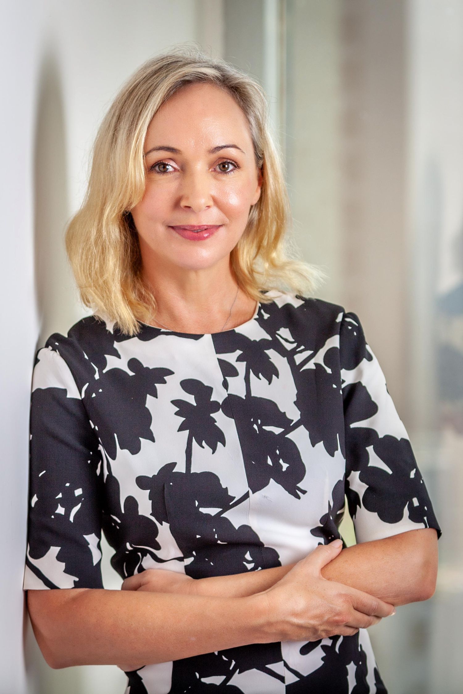 Professional portrait of someone in a black and white floral dress with short blonde hair and a friendly expression.