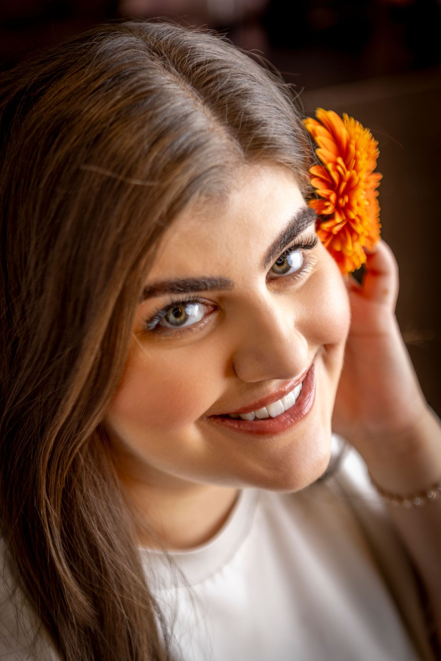 A bright orange marigold flower adorns dark brown hair against a blurred background.