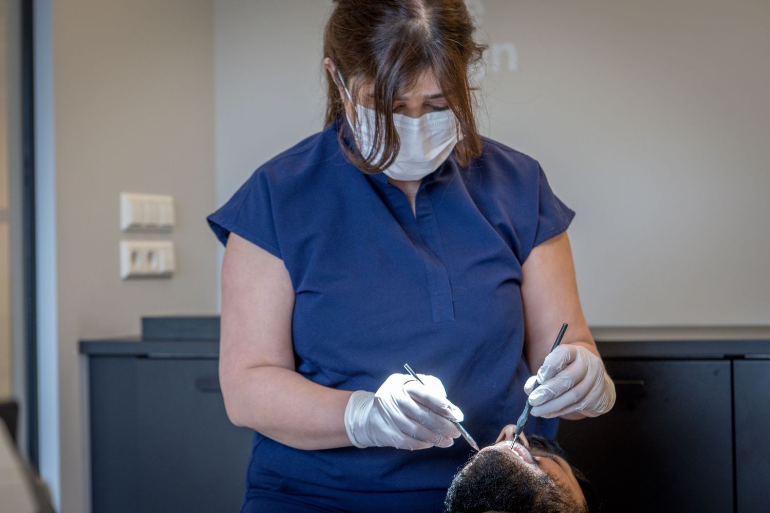 A dental hygienist wearing protective gear performs a dental cleaning procedure in a clinical setting.