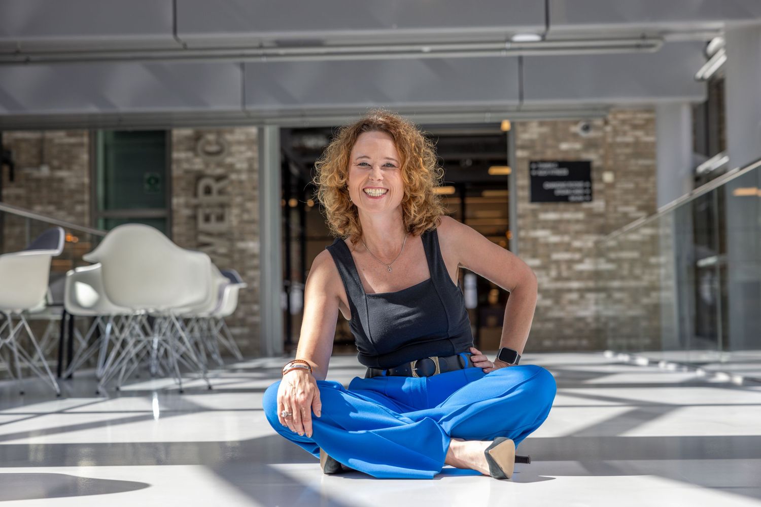 Looking relaxed in bright, modern office space with someone seated cross-legged on floor wearing blue pants.