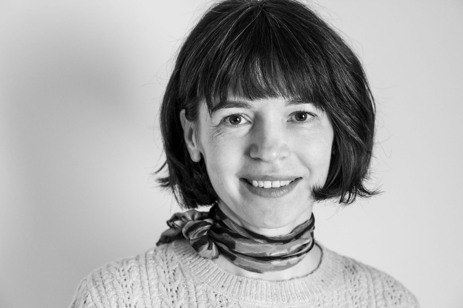 Black and white portrait of a person with a short bob haircut wearing a sweater with a scarf tied around her neck.