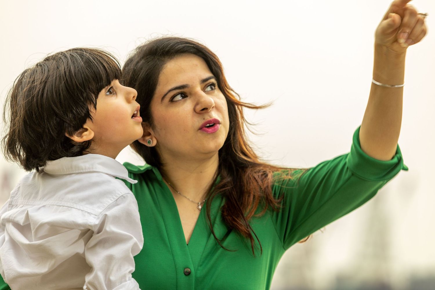 A young mother wearing a green shirt pointing upward while her young son other looks at whatever she's pointing at.