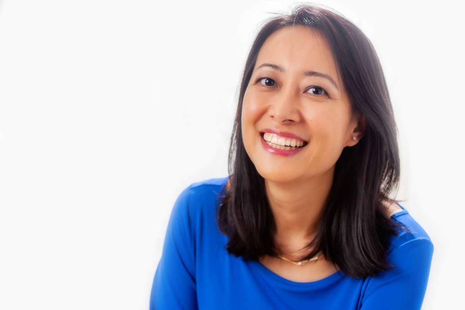 A smiling person wearing a bright blue sweater glances to the side while posing against a white background.