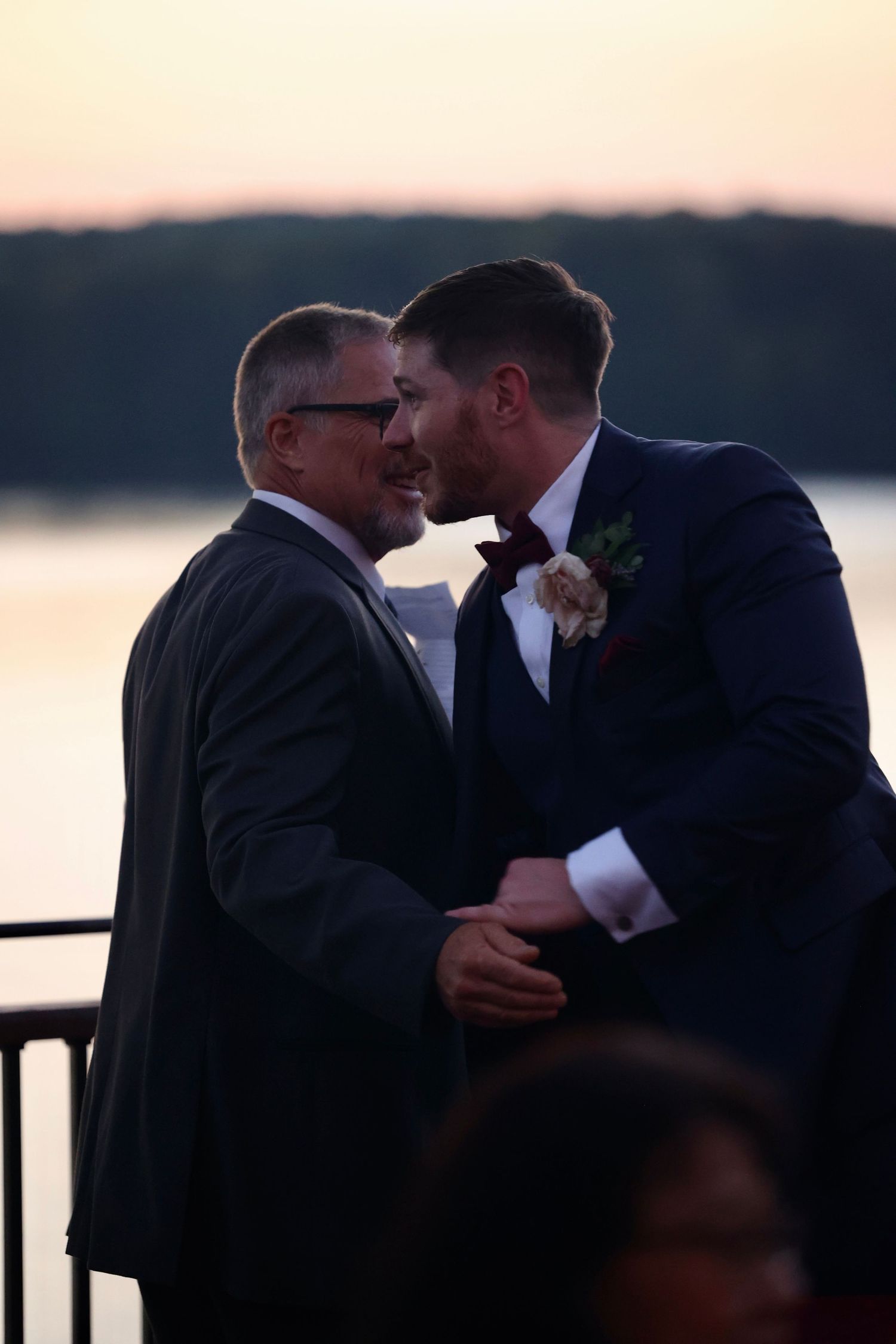 Two grooms sharing moment during a waterfront sunset wedding ceremony