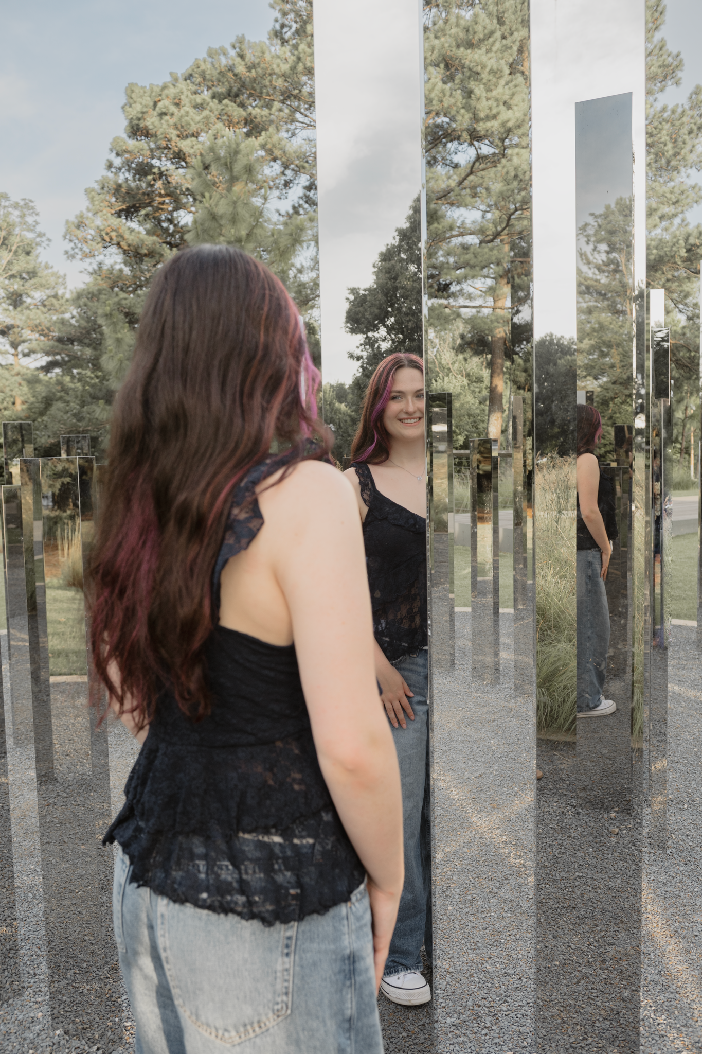 A reflective art installation with mirrored columns creates an interesting visual effect in a wooded outdoor setting for a senior session