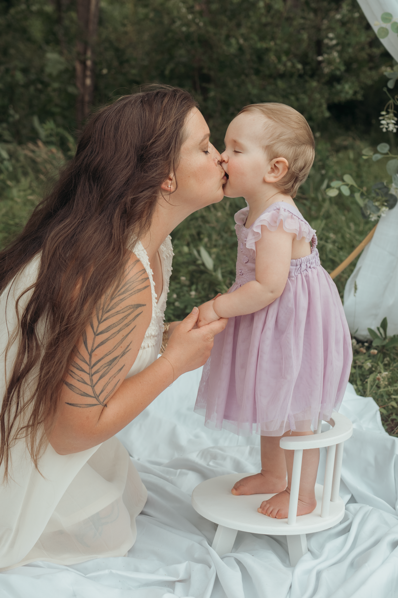 A tender moment shared outdoors against a natural backdrop with white fabric and greenery in the background.