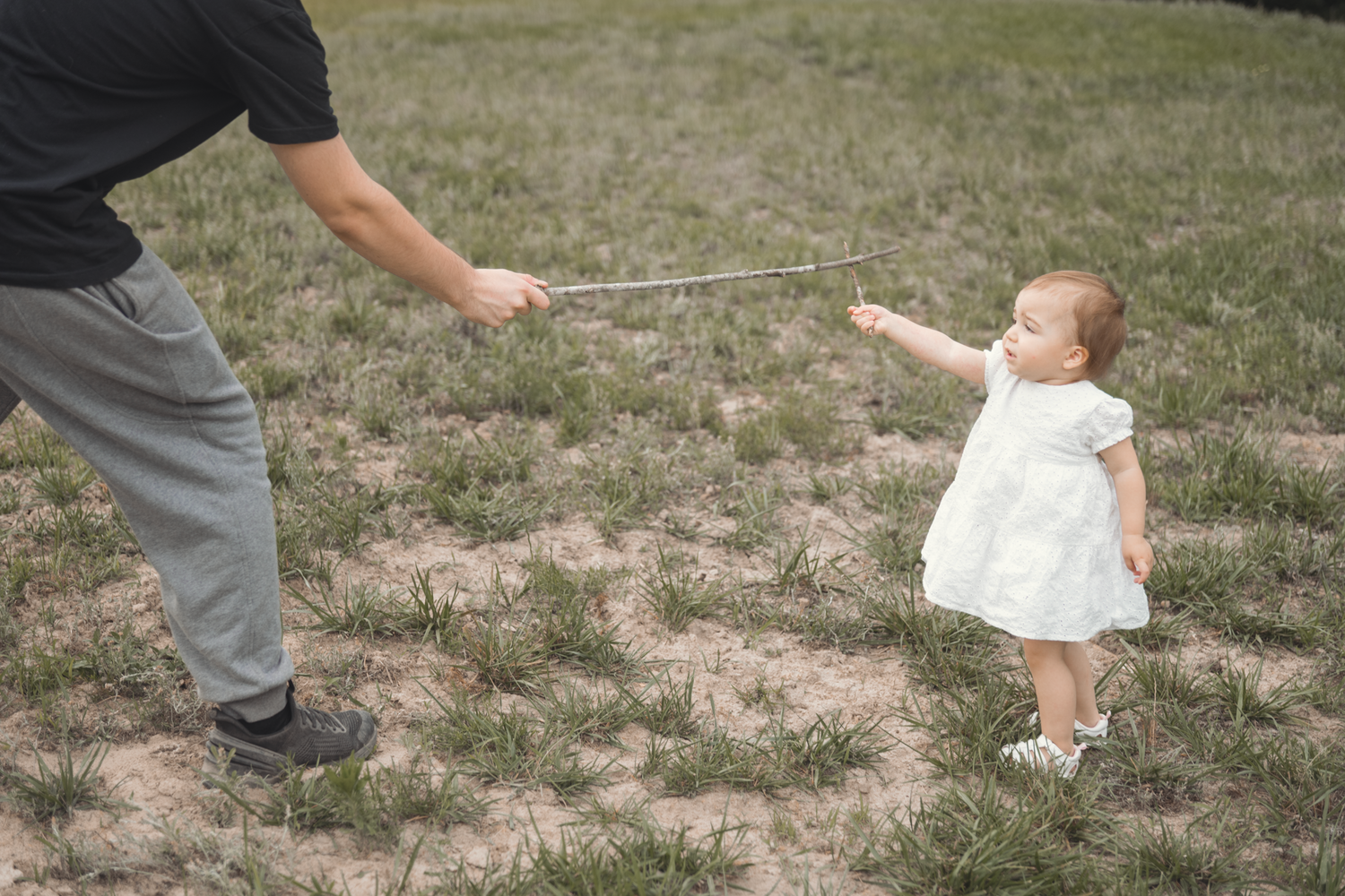 A person in white dress stands in grass while holding a stick with someone outside the frame.