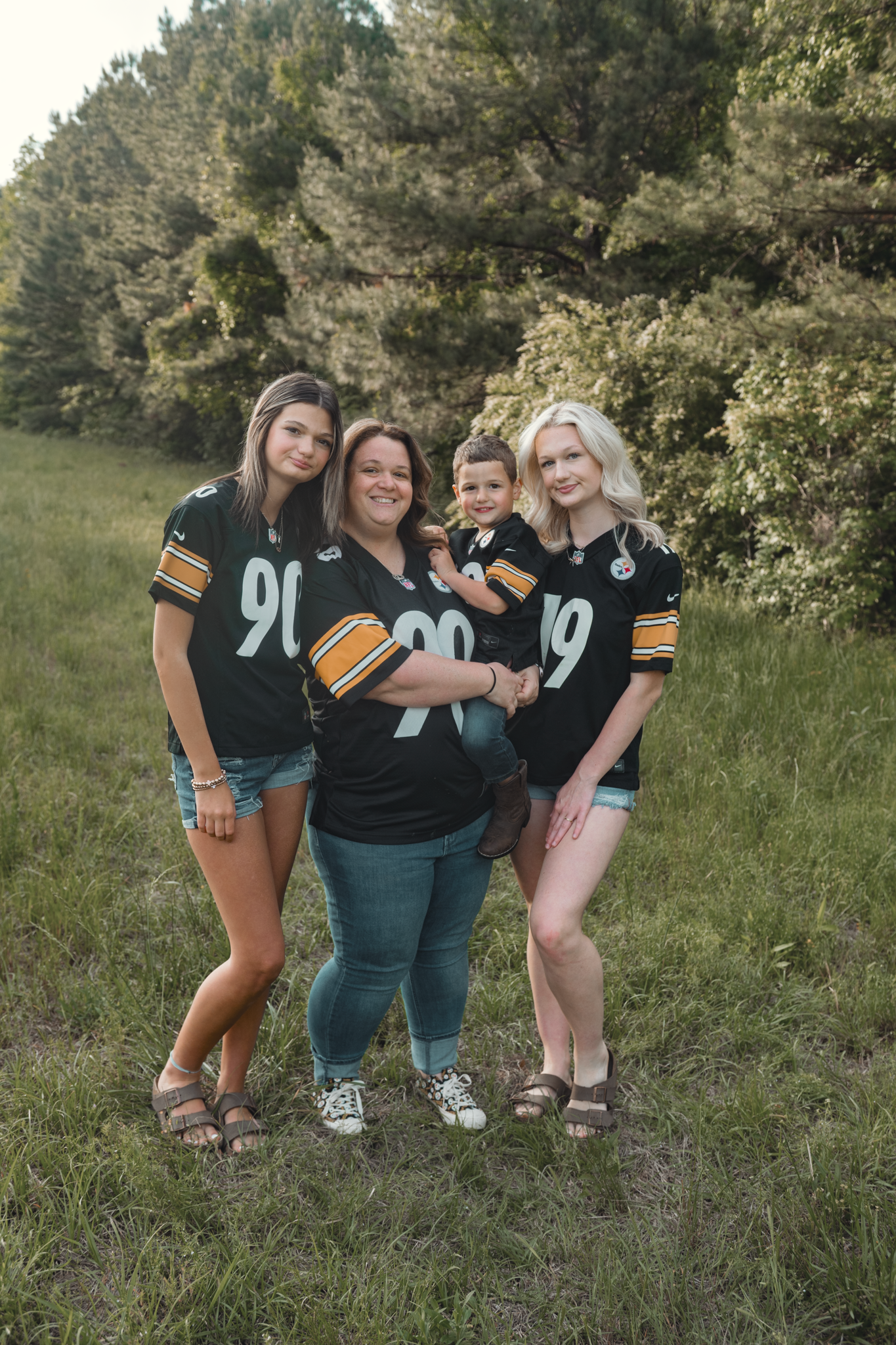 Group wearing black and gold sports jerseys pose together in a grassy outdoor setting with trees in background.