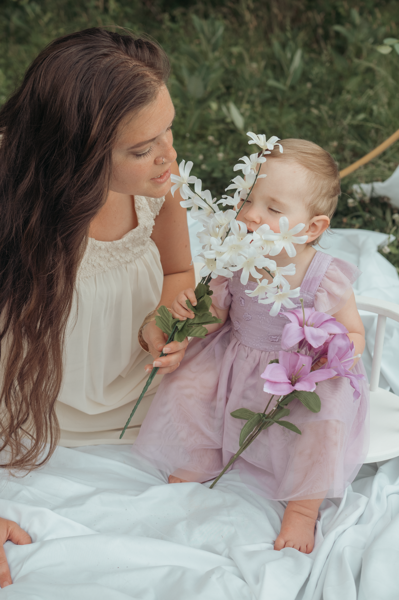A peaceful moment shared with white lilies and pink flowers on a white blanket in a natural setting.