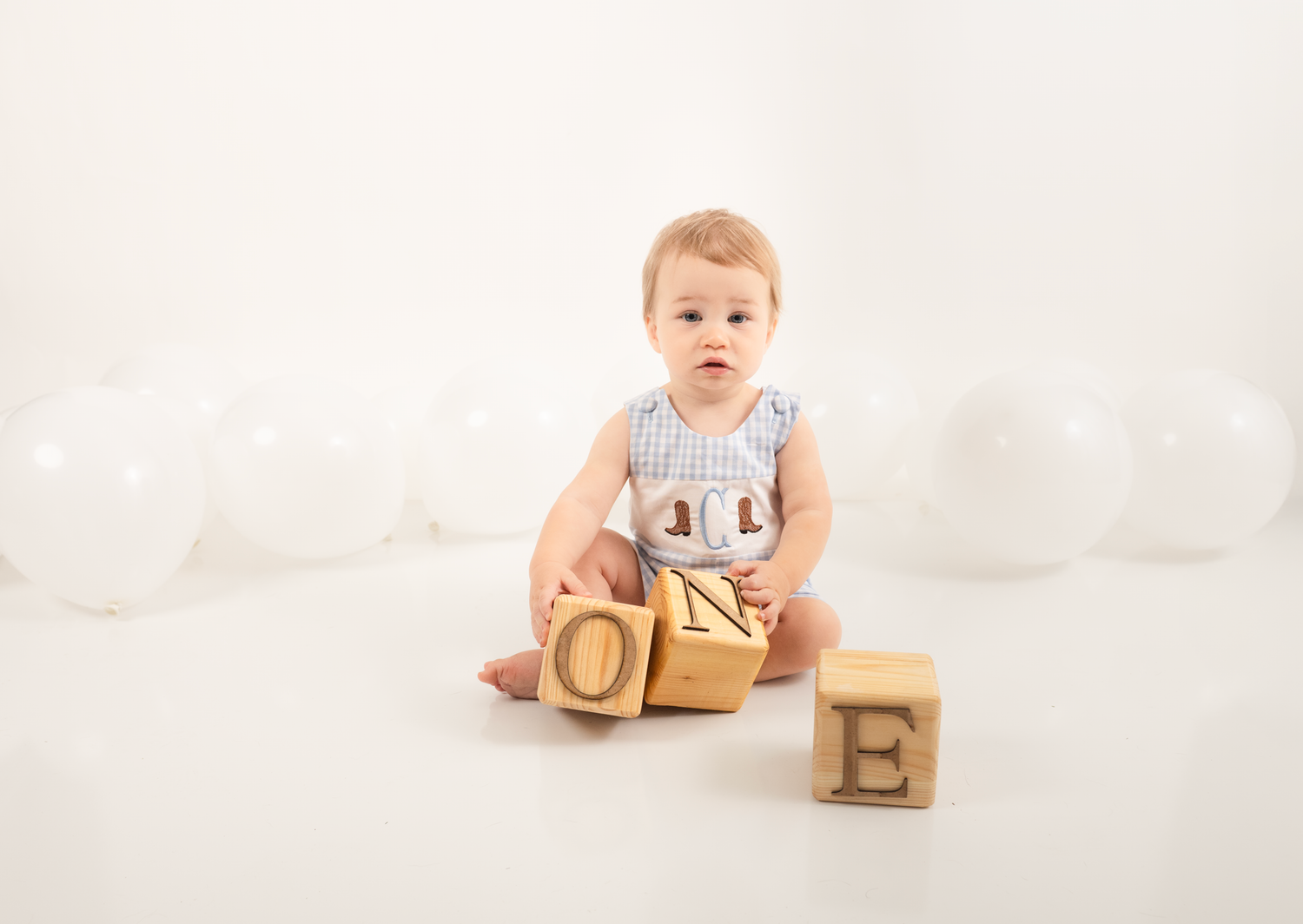 Baby sits in white studio setting with wooden alphabet blocks displaying developmental milestone photography.