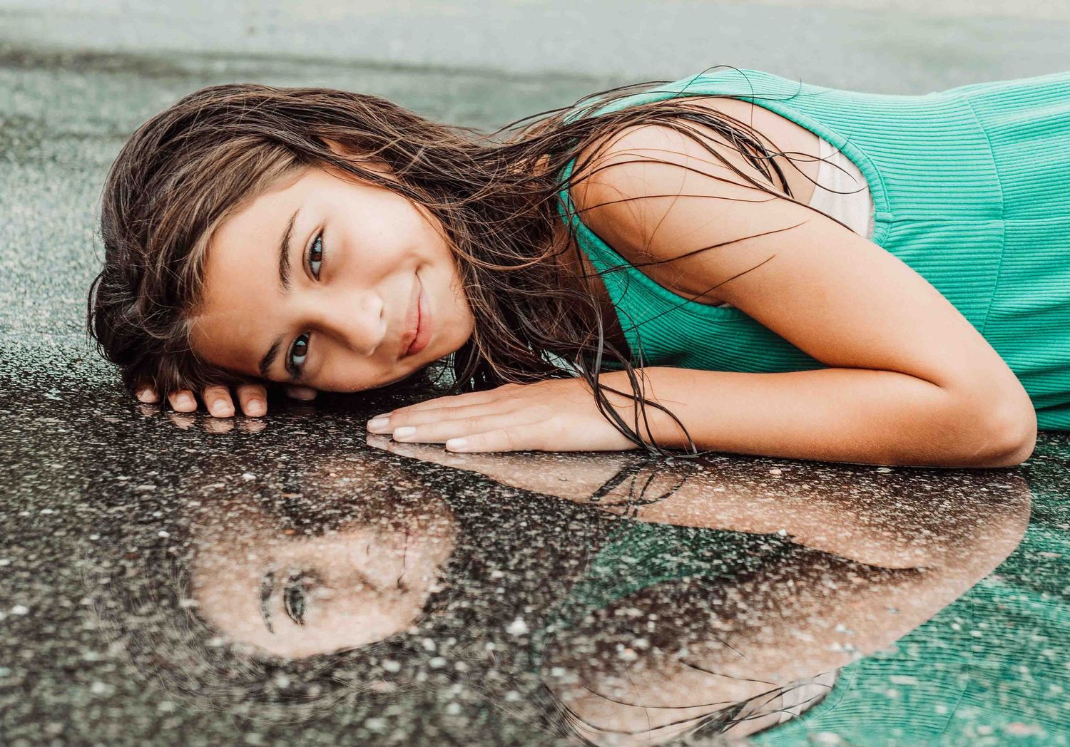 A series of artistic portraits showing someone lying on textured ground wearing a turquoise dress.