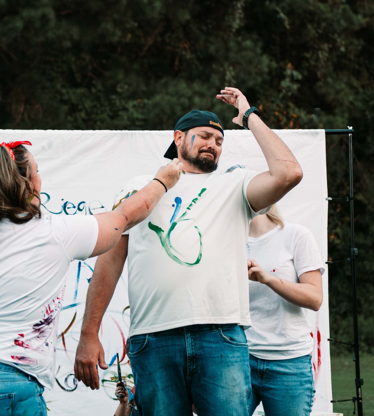 People in white t-shirts playing a paint splatter team building game outdoors with colorful paint markings.
